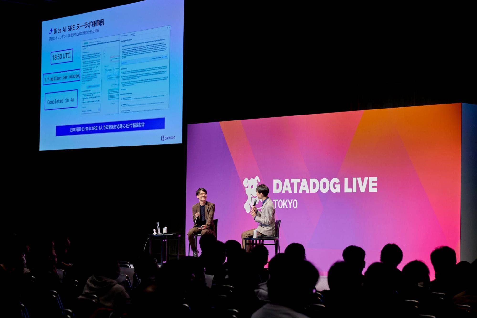 Datadog Live Tokyo 2025 にて、登壇者がステージ上でBits AI SRE に関するスライドを表示しながら対談する様子。