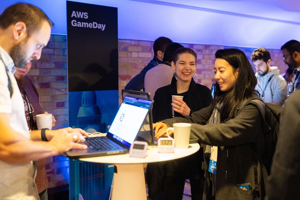 People stand at elevated tables and use their laptops to participate in AWSGameDay. People stand at elevated tables and use their laptops to participate in AWSGameDay.