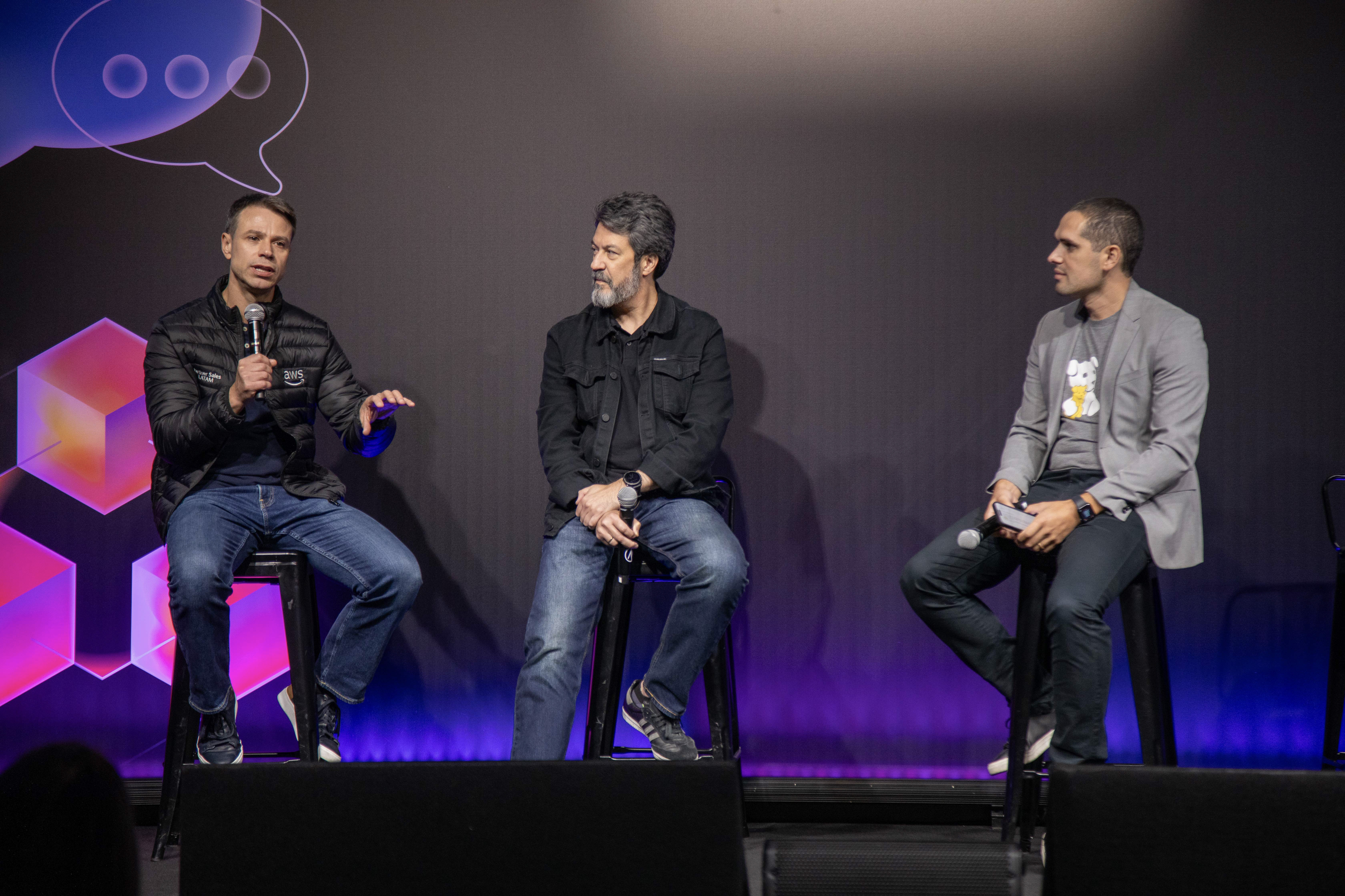Three speakers seated on stage with microphones during a panel discussion.